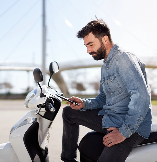 Spanish man using cell phone or smartphone sitting on his motor scooter outdoors in the city