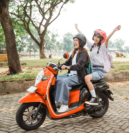 Two students wearing helmets and jackets riding motorbikes