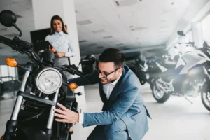 Saleswoman helping a man inspecting a new motorbike in a showroom, looking to finance a new motorbike