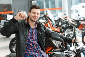 Cheerful owner. Shot of a stunning handsome young man sitting on his new motorbike holding keys smiling to the camera cheerfully at the motorcycle salon